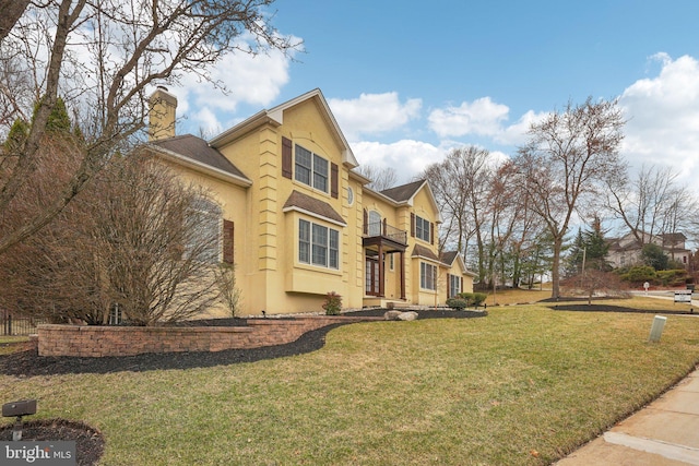 view of side of property featuring a balcony, a chimney, a yard, stucco siding, and roof with shingles