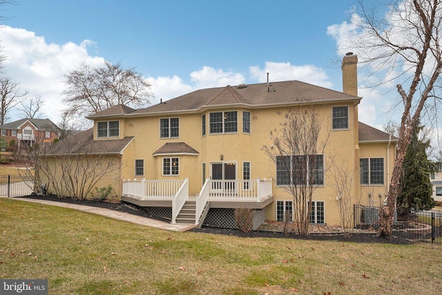 back of house featuring a chimney, a lawn, fence, stucco siding, and a wooden deck