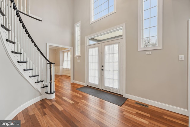 foyer entrance featuring stairway, a high ceiling, visible vents, wood-type flooring, and baseboards