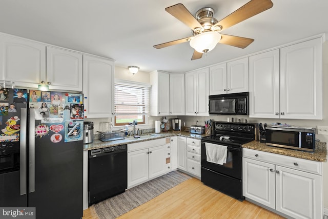 kitchen with white cabinets, a sink, black appliances, light wood finished floors, and stone counters