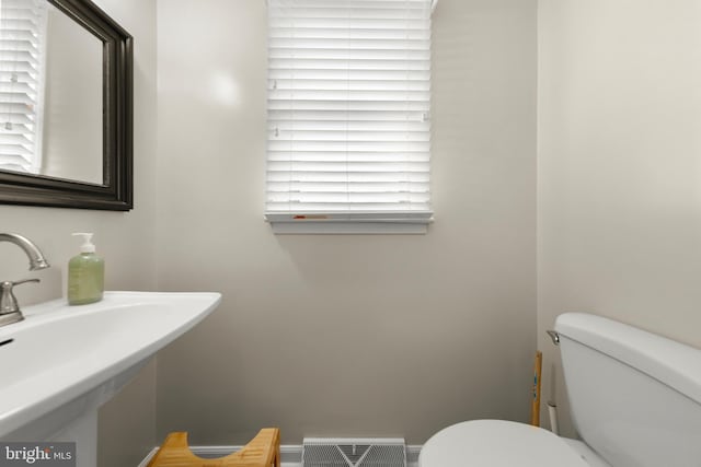 half bathroom featuring baseboards, visible vents, toilet, and a sink