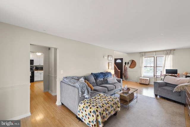 living room with baseboards, light wood-type flooring, and stairs