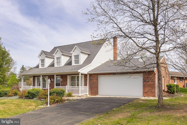 new england style home with aphalt driveway, a chimney, covered porch, brick siding, and a garage
