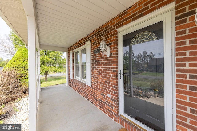 doorway to property featuring a porch and brick siding