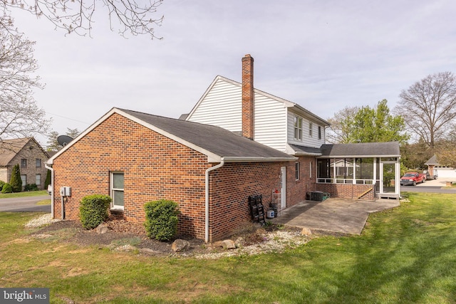 rear view of property with a patio, a chimney, a lawn, brick siding, and a sunroom