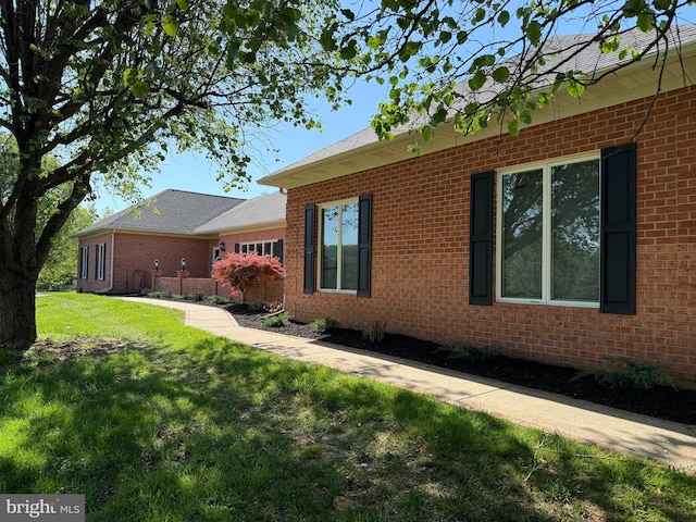 view of side of property with brick siding, a lawn, and roof with shingles