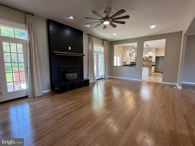 unfurnished living room featuring a ceiling fan, a tiled fireplace, wood finished floors, baseboards, and recessed lighting