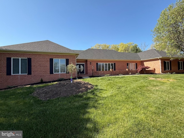 back of house with a lawn, roof with shingles, and brick siding
