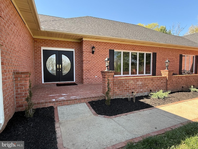property entrance with brick siding, a shingled roof, and french doors