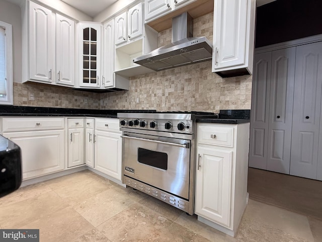 kitchen featuring dark countertops, tasteful backsplash, wall chimney exhaust hood, white cabinetry, and luxury range