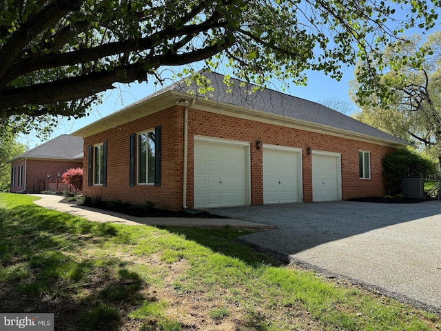 view of side of home with brick siding, central AC unit, an attached garage, and driveway