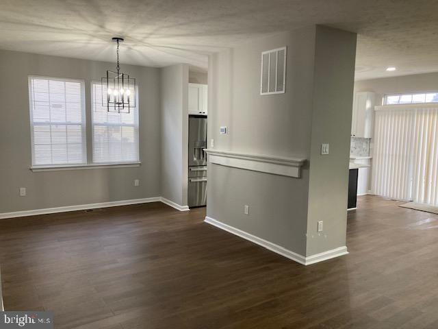 unfurnished dining area with baseboards, visible vents, a chandelier, and dark wood finished floors