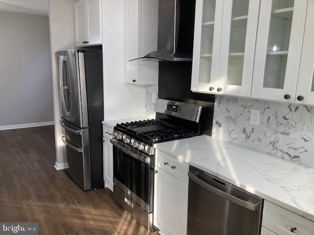kitchen with white cabinets, wall chimney exhaust hood, appliances with stainless steel finishes, and light stone countertops
