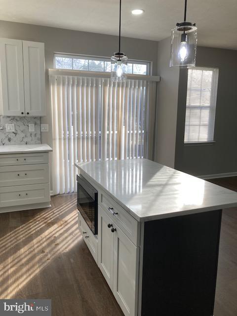kitchen with dark wood-type flooring, light countertops, black microwave, and white cabinets