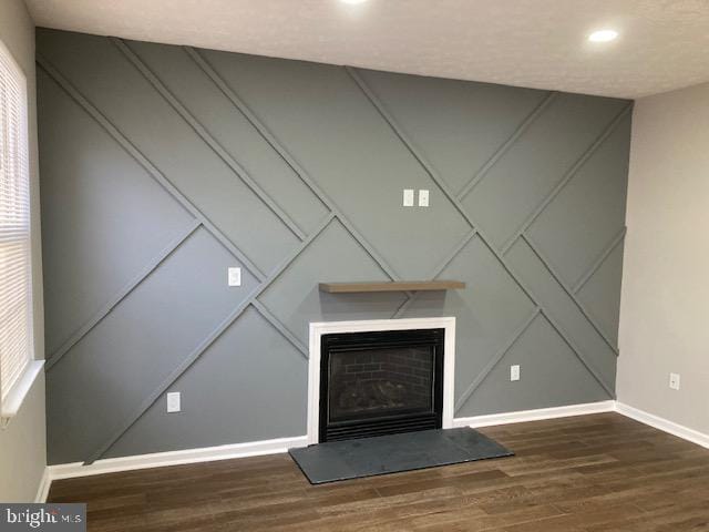 interior details with a fireplace with raised hearth, wood finished floors, a decorative wall, and baseboards