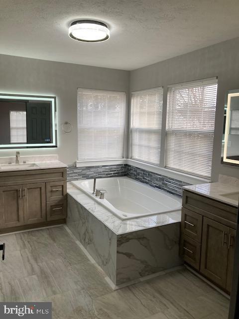 bathroom featuring two vanities, a garden tub, a sink, and a textured ceiling
