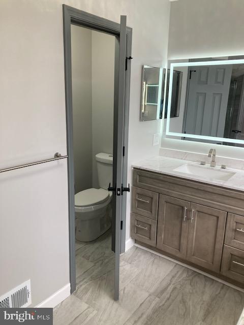 bathroom featuring toilet, vanity, visible vents, and baseboards