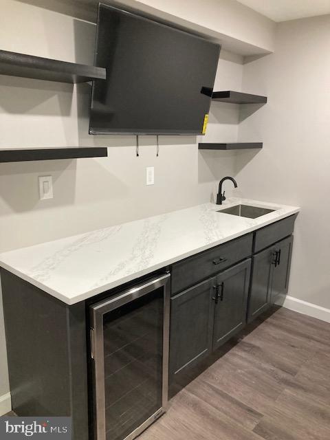 kitchen with beverage cooler, open shelves, wood finished floors, a sink, and baseboards