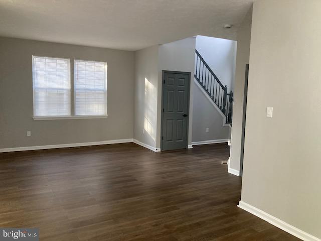 unfurnished living room with baseboards, stairway, and dark wood-style flooring