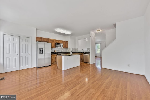 kitchen with dark countertops, open floor plan, a sink, light wood finished floors, and stainless steel appliances
