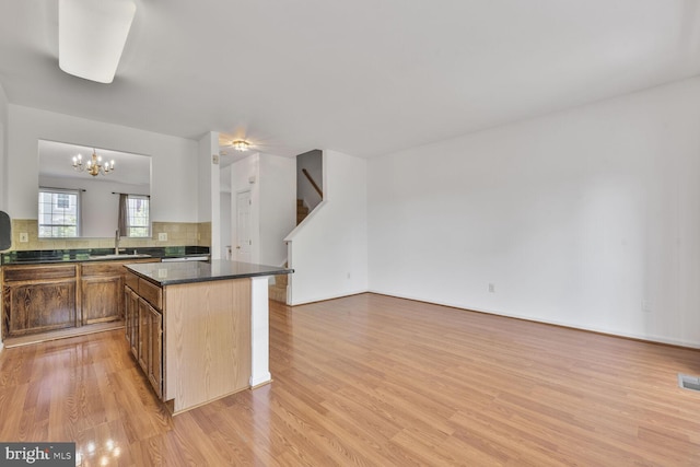 kitchen featuring dark countertops, open floor plan, light wood-type flooring, a sink, and backsplash