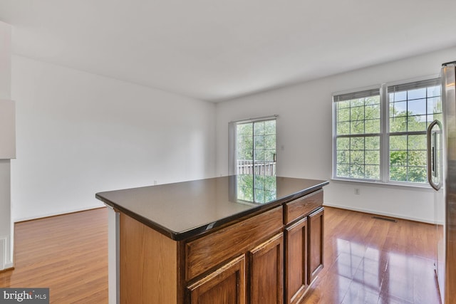 kitchen featuring dark countertops, a center island, brown cabinets, baseboards, and light wood-style floors