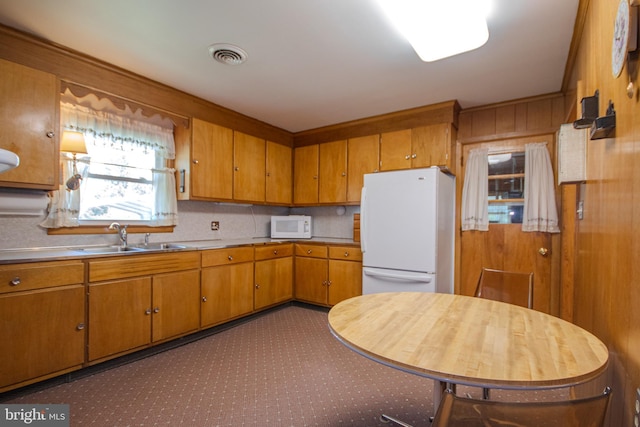 kitchen with a sink, white appliances, brown cabinetry, visible vents, and light countertops