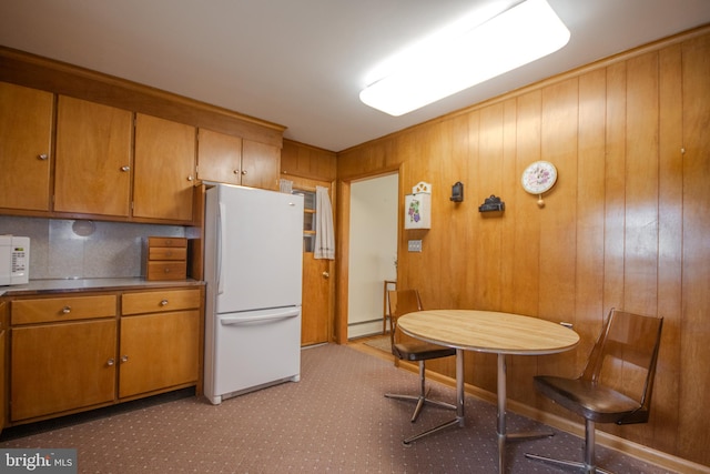 kitchen featuring carpet flooring, baseboard heating, wooden walls, white appliances, and brown cabinetry