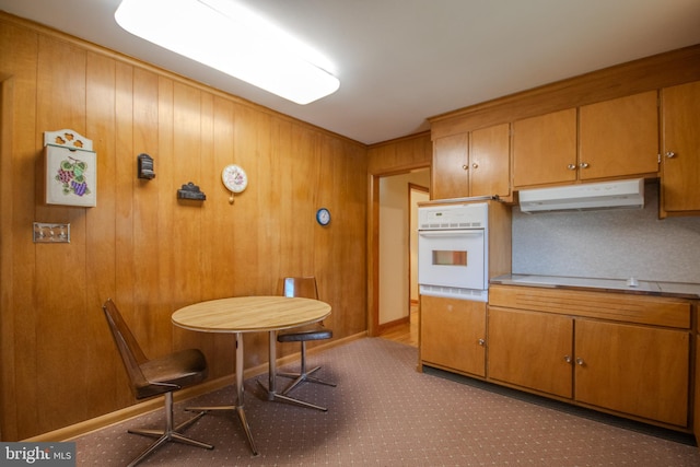 kitchen with white oven, brown cabinets, under cabinet range hood, and wood walls