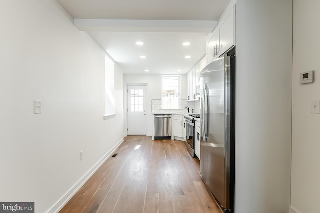 kitchen featuring backsplash, light wood-style floors, baseboards, appliances with stainless steel finishes, and white cabinetry