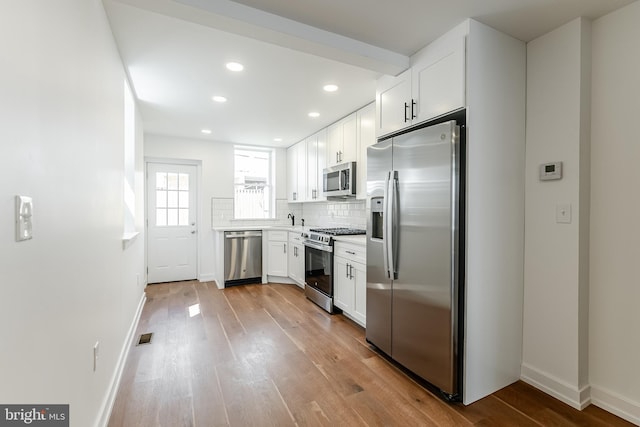 kitchen featuring white cabinets, baseboards, wood finished floors, and stainless steel appliances