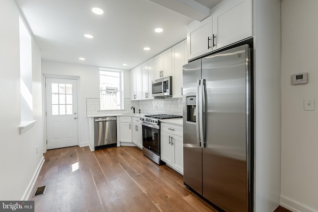 kitchen with a sink, white cabinetry, dark wood finished floors, appliances with stainless steel finishes, and visible vents