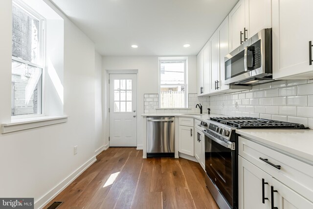 kitchen with stainless steel appliances, a sink, baseboards, backsplash, and wood finished floors