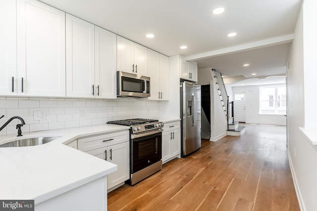 kitchen with light wood-style floors, appliances with stainless steel finishes, baseboards, and a sink