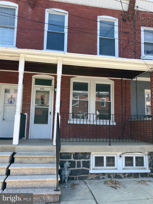 view of exterior entry featuring a porch and brick siding