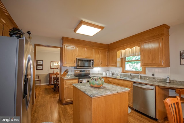 kitchen with a sink, stainless steel appliances, light stone counters, a center island, and light wood-style floors