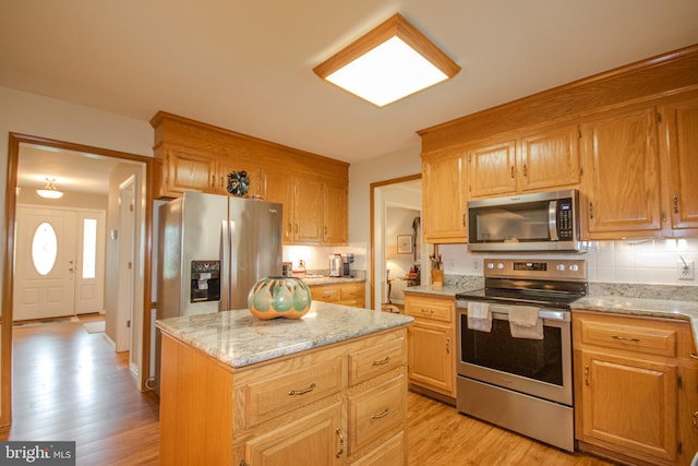 kitchen with stainless steel appliances, light stone counters, light wood-type flooring, decorative backsplash, and a center island