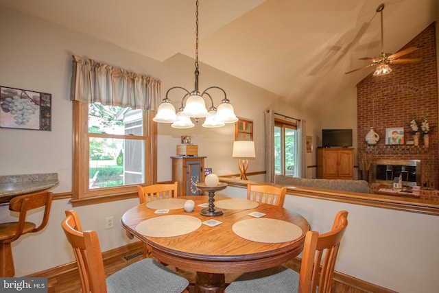 dining room featuring lofted ceiling, ceiling fan with notable chandelier, wood finished floors, a fireplace, and baseboards