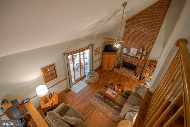 living area featuring lofted ceiling, a brick fireplace, ceiling fan, and wood finished floors