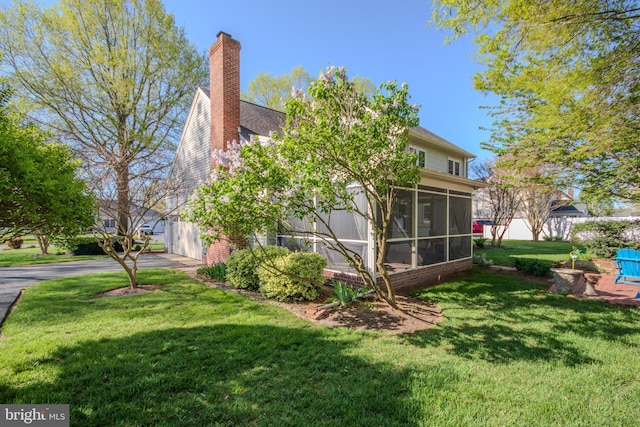 exterior space featuring a sunroom, a chimney, and a lawn