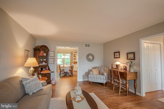 living area with a chandelier, baseboards, visible vents, and wood finished floors