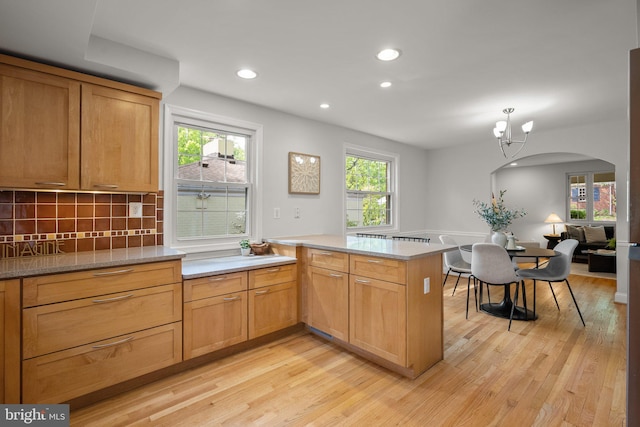 kitchen featuring backsplash, arched walkways, a peninsula, light wood-style floors, and recessed lighting