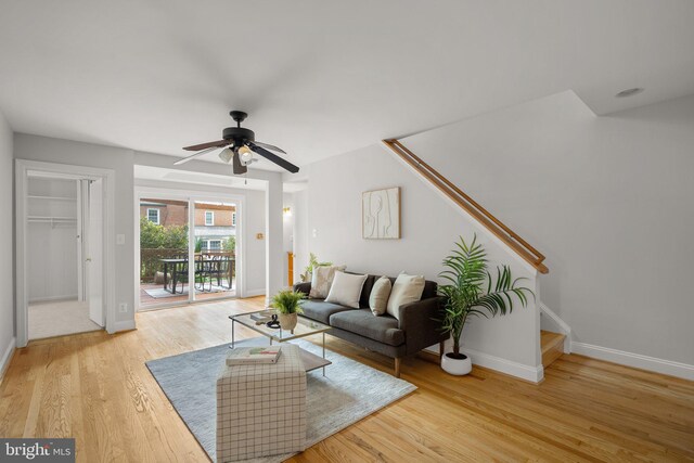 living room featuring stairs, a ceiling fan, baseboards, and light wood finished floors