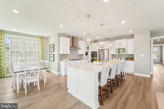 kitchen with decorative backsplash, a chandelier, appliances with stainless steel finishes, light countertops, and wall chimney range hood