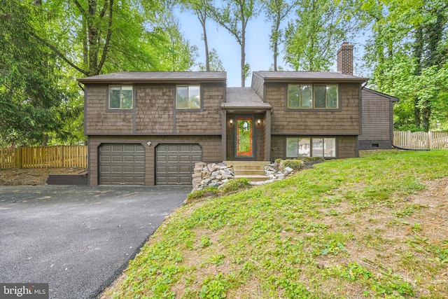 split foyer home featuring a garage, fence, a chimney, and aphalt driveway