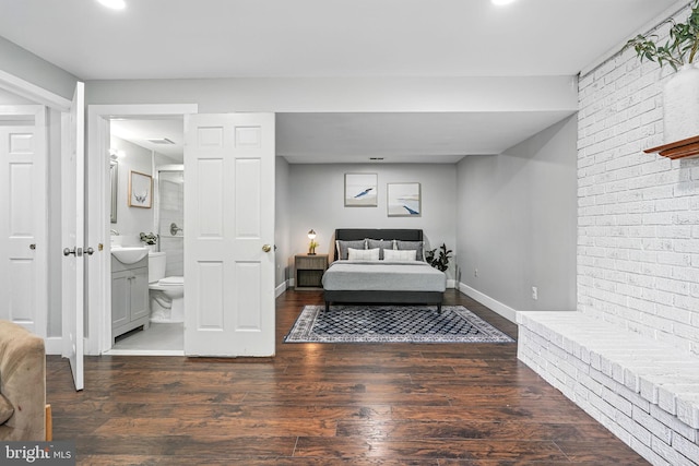 bedroom featuring baseboards, ensuite bath, wood finished floors, and brick wall