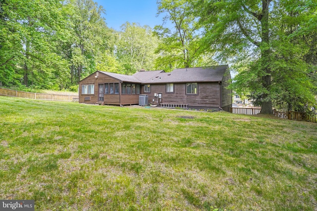 rear view of house with a lawn, a fenced backyard, a sunroom, and central air condition unit