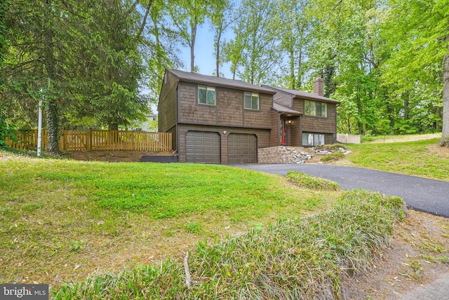 split foyer home with driveway, a chimney, a garage, fence, and a front lawn