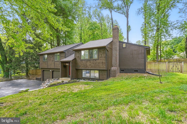 split foyer home with a garage, a front lawn, aphalt driveway, fence, and a chimney