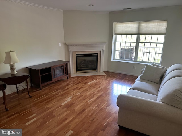 living area featuring visible vents, ornamental molding, wood finished floors, baseboards, and a fireplace with flush hearth